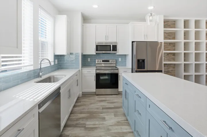 Modern kitchen featuring white cabinetry, a light blue island, stainless steel appliances, a subway tile backsplash, and light wood-finish flooring