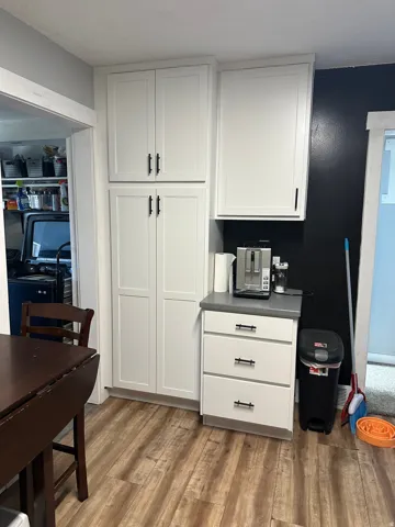 White shaker-style cabinetry with matte black hardware, grey countertop, and wood-finish flooring