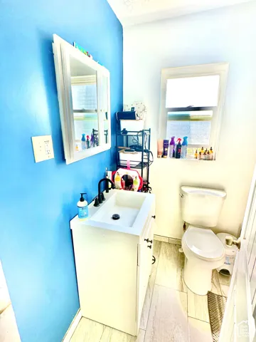 White vanity with a rectangular basin, matte black widespread faucet, medicine cabinet, and wood-finish flooring