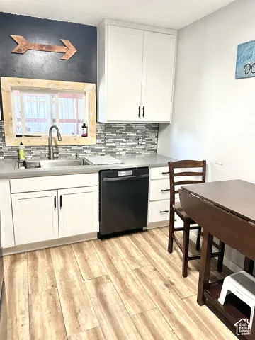Kitchen featuring white Shaker-style cabinetry, multi-tonal linear tile backsplash, stainless steel sink with high-arc faucet, and wood-finish flooring
