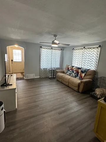 Spacious living area featuring wood-finish flooring, a ceiling fan with integrated lighting, and light gray wall paint