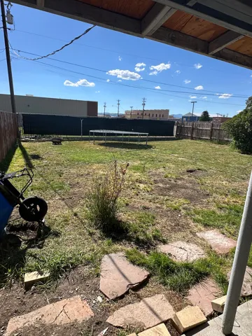Expansive outdoor space featuring a large grassy area, partial wood privacy fencing, and a covered patio structure with exposed wood beams