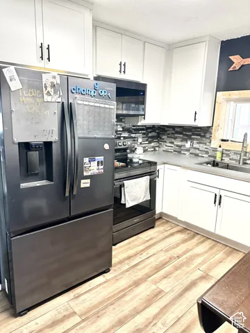 Kitchen featuring white shaker-style cabinetry, dark stainless steel appliances, multi-tonal mosaic tile backsplash, solid-surface countertops, and wood-finish flooring