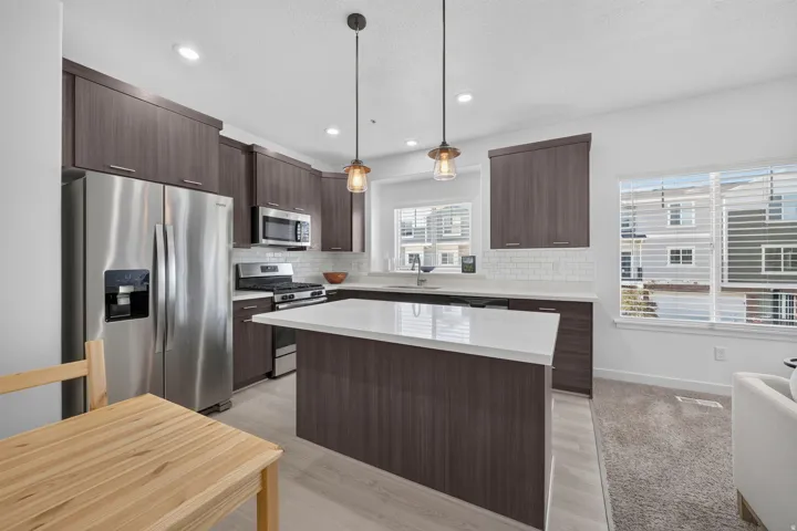 Contemporary kitchen featuring dark wood-finish cabinetry, stainless steel appliances, a white subway tile backsplash, and light wood-finish flooring
