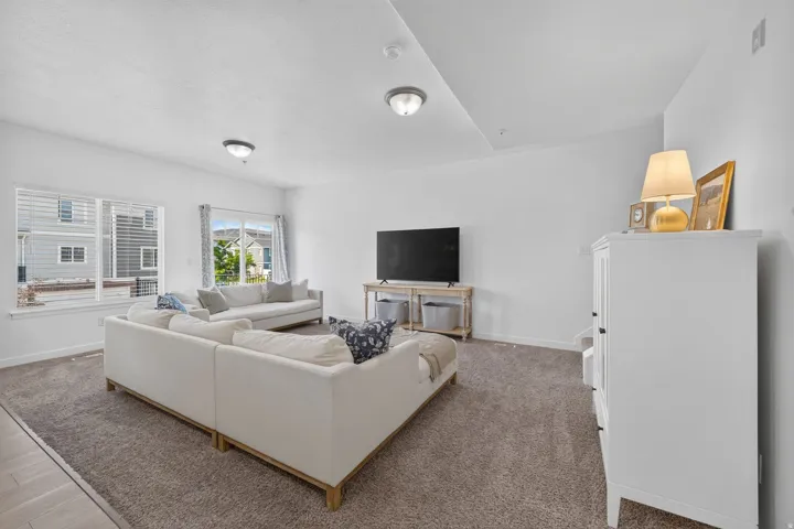 Spacious living area featuring neutral carpeting, white walls, multiple windows with blinds, and recessed lighting