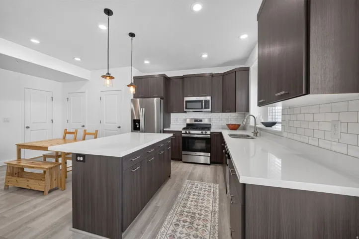 Contemporary kitchen featuring wood-finish cabinetry, light countertops, and stainless steel appliances