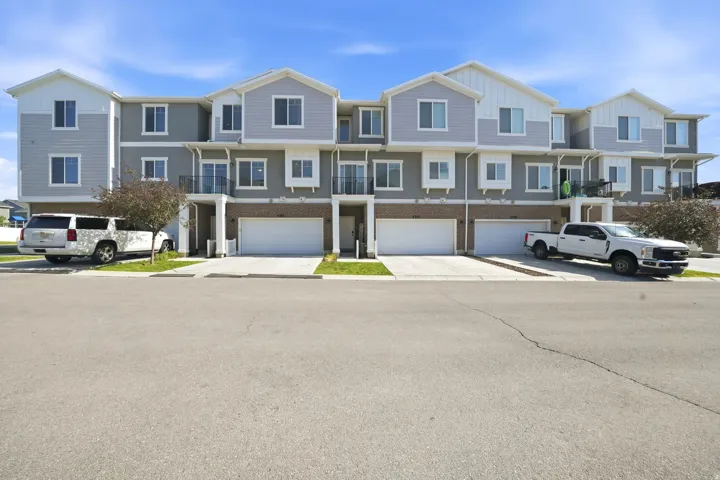 Contemporary townhome exterior featuring multi-level construction, light grey siding with white trim accents, individual garage doors, and private balconies with black railings