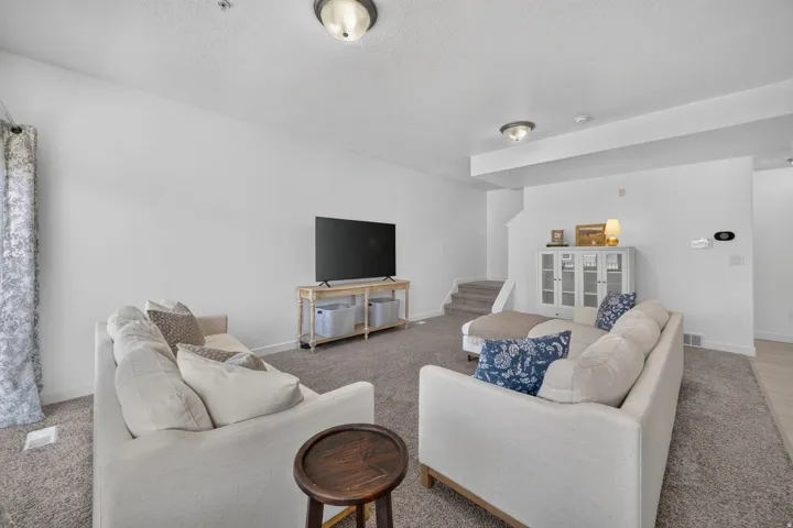Spacious living area featuring neutral carpeting, white painted walls, and ceiling-mounted light fixtures