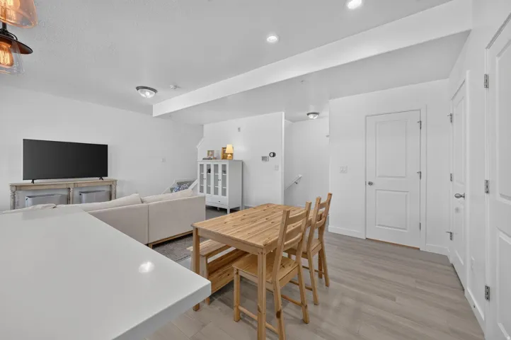 Open-concept living area featuring light wood-finish flooring, white walls, recessed lighting, and a white kitchen island counter