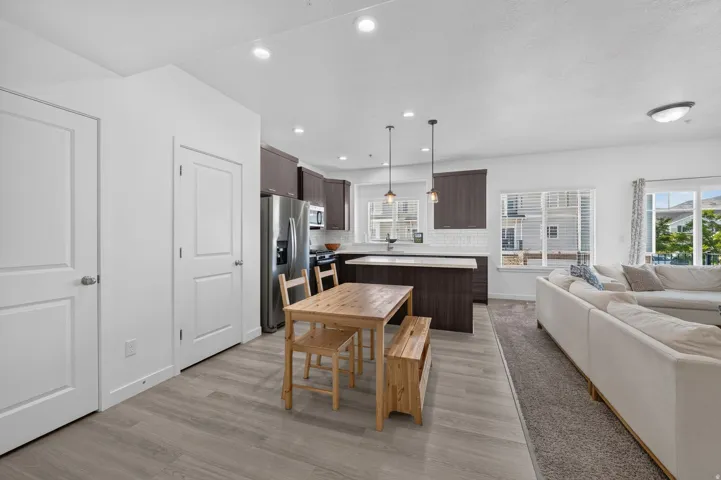 Open-concept kitchen and living area featuring wood-finish flooring, recessed lighting, dark wood cabinetry, stainless steel appliances, and a white subway tile backsplash