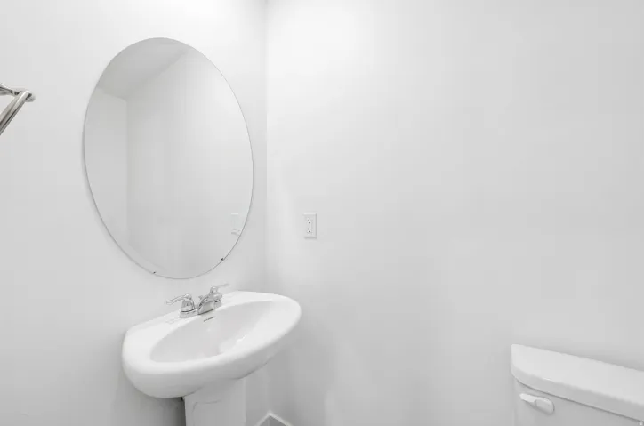 Pedestal sink with chrome faucet, complemented by an oval wall-mounted mirror