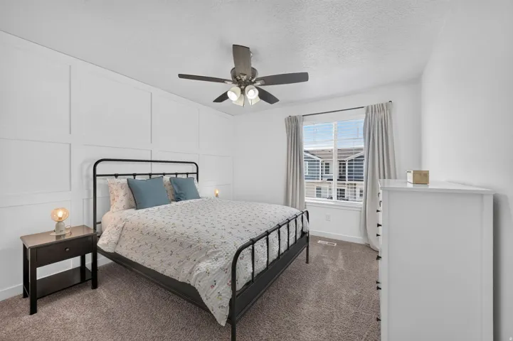 Carpeted room featuring a white accent wall with panel detailing, a window with horizontal blinds and drapes, and a ceiling fan with integrated lighting