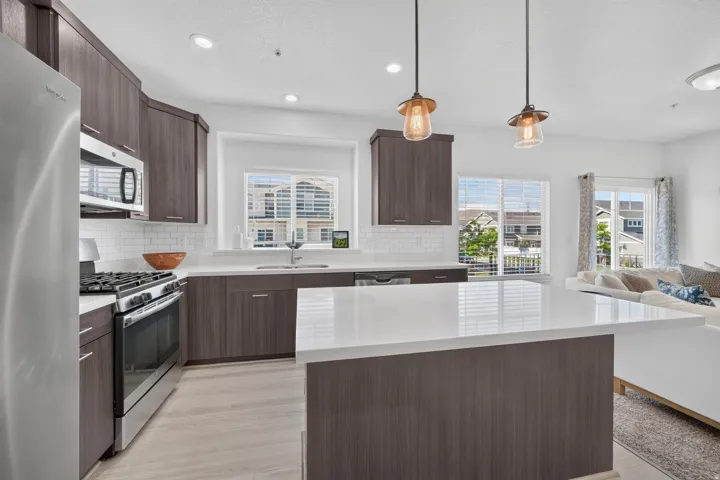 Modern kitchen featuring a central island with a light-toned countertop, wood-finish cabinetry, stainless steel appliances, a subway tile backsplash, and recessed lighting