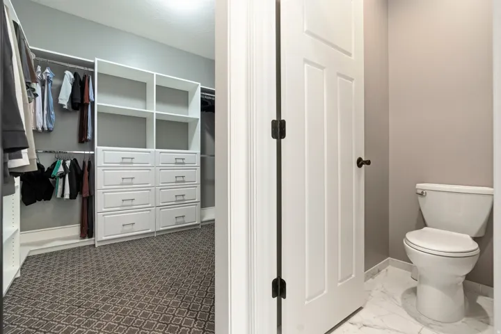 Walk-in closet featuring built-in white cabinetry, integrated shelving, and patterned carpet flooring
