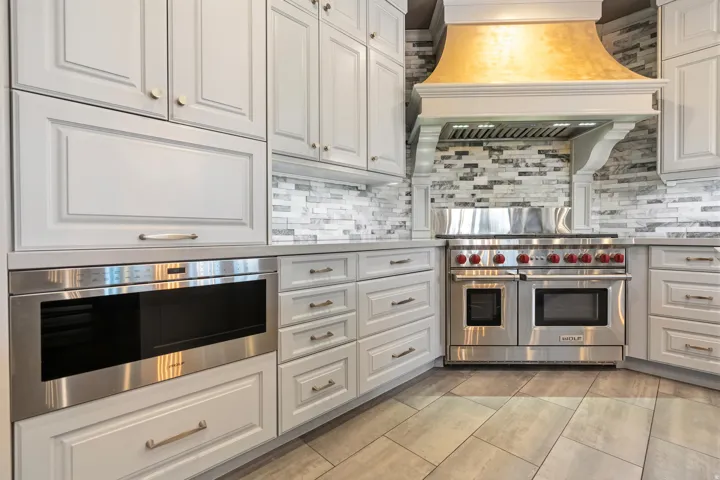 Gourmet kitchen featuring a professional-grade stainless steel range with double ovens, custom decorative range hood, light-toned cabinetry, stone tile backsplash, and wood-finish flooring