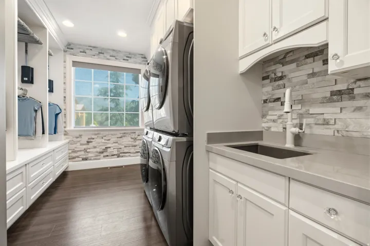 Dedicated laundry room featuring stacked washer and dryer units, a utility sink with a white faucet, and extensive white cabinetry