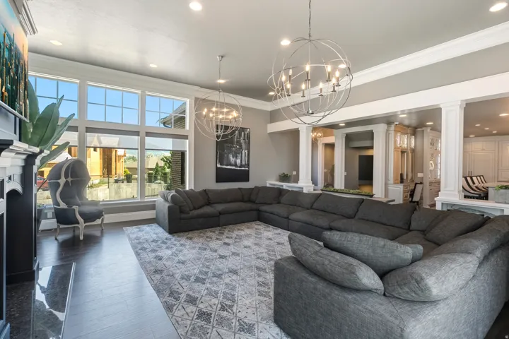 Spacious living area featuring large windows, dark wood-finish flooring, recessed lighting, and decorative chandeliers