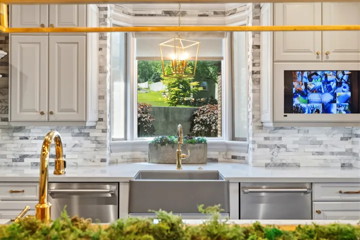 Kitchen sink area featuring a deep farmhouse-style sink, gold-finish faucet, and stainless steel dishwasher
