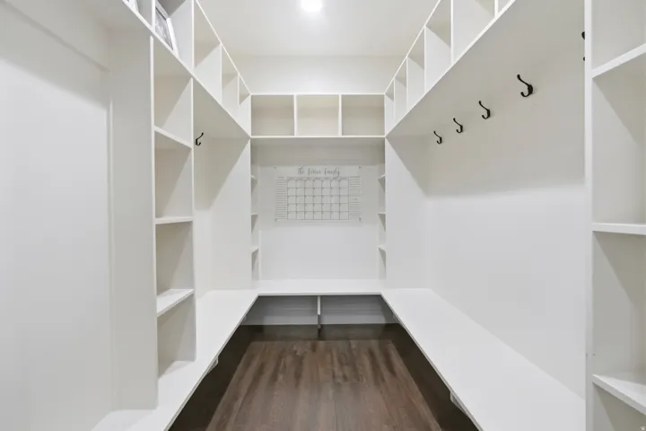 Built-in storage area with dark wood-finish flooring, white shelving units, integrated bench seating, and wall-mounted hooks