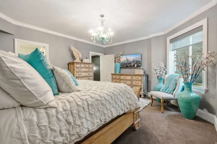 Carpeted room featuring a large window with roller shades, crown molding, and a chandelier light fixture