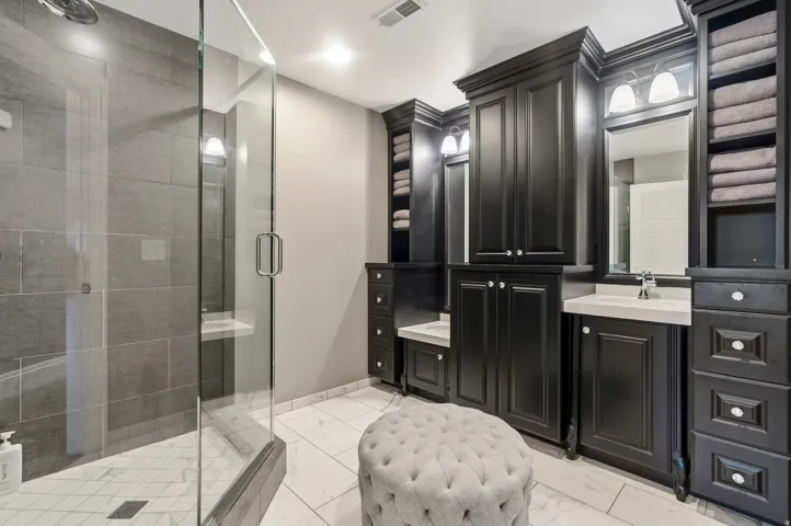 Spacious bathroom featuring a glass-enclosed shower with gray tiled walls and a built-in bench and children sinks
