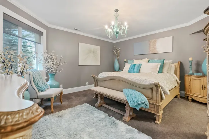 Spacious room featuring gray walls, crown molding, a large window with roller shades, and a chandelier lighting fixture