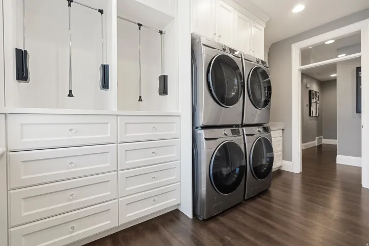 Custom built-in cabinetry featuring white shaker-style drawers with crystal knobs, pull-down hanging rods, and integrated stacked laundry appliances