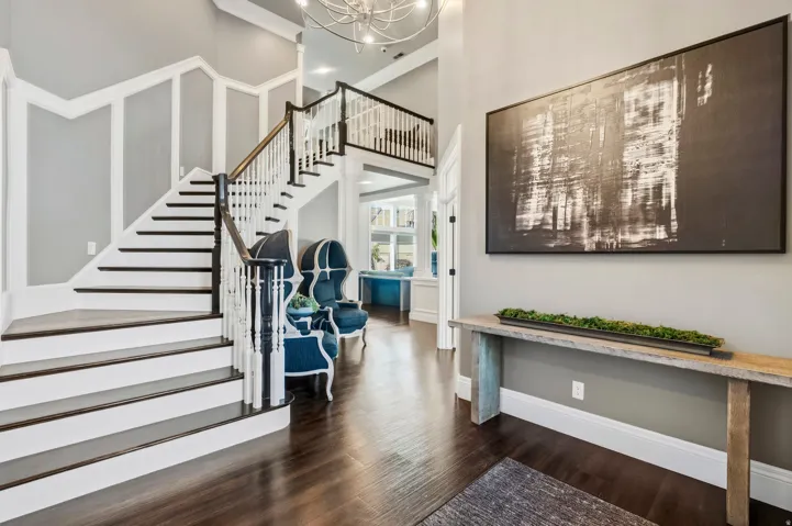 Grand foyer featuring a two-story staircase with dark wood treads and white risers, wood-finish flooring, and wainscoting details