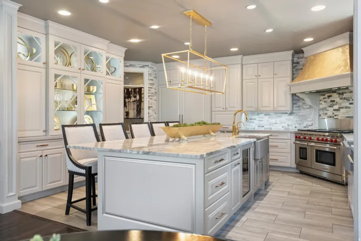 Gourmet kitchen featuring a large central island with a stone countertop, a gold-toned linear chandelier, white cabinetry with glass-front accents, stainless steel range, and a gold-toned range hood