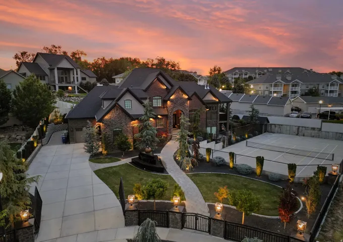 Stone and brick exterior residence featuring a paved driveway, front lawn, and mature landscaping