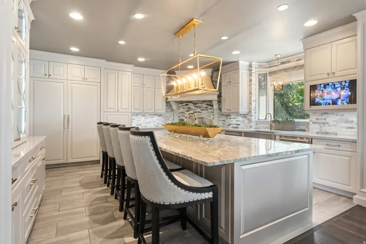 Spacious kitchen featuring a large central island with seating for six, extensive white cabinetry, integrated appliances, a decorative tile backsplash, and recessed lighting