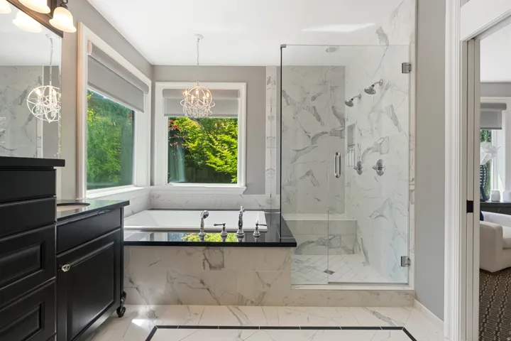 Spacious bathroom featuring a built-in soaking tub, a frameless glass shower with a built-in bench and multiple showerheads, extensive marble-patterned tile, and dual windows
