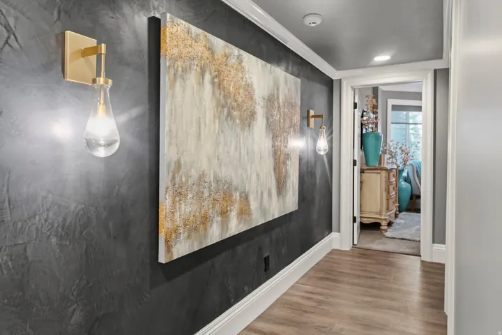 Hallway featuring wood-finish flooring, dark textured wall accents, white crown molding, and contemporary brass sconces