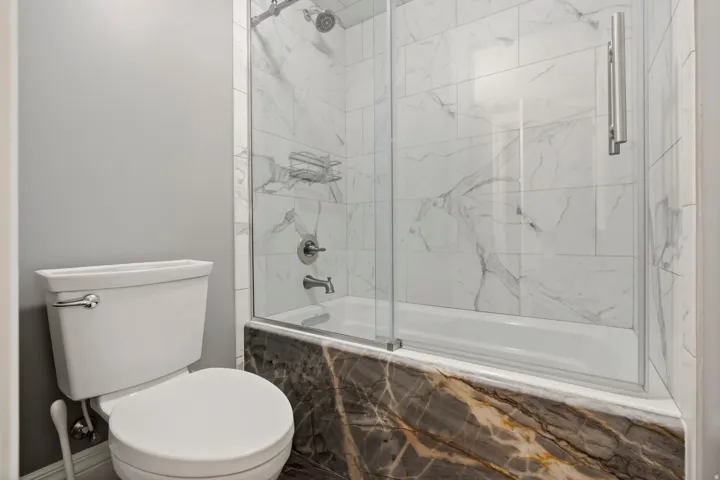 Bathroom featuring a white toilet, gray wall paint, and a shower-over-tub combination