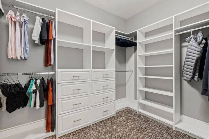 Custom closet system featuring multiple hanging rods, integrated drawers with brushed nickel hardware, open shelving, and patterned carpet flooring