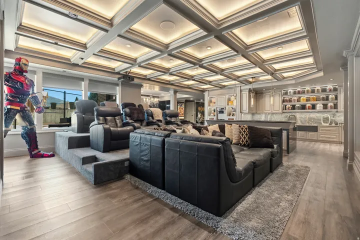 Entertainment room featuring a coffered ceiling with integrated lighting, tiered seating, wood-finish flooring, a built-in wet bar with cabinetry, and a projector