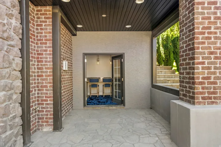 Covered outdoor patio with stamped concrete flooring, brick and stone veneer accents, and a dark wood slat ceiling with recessed lighting