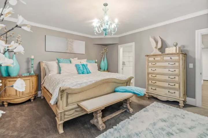 Bedroom featuring a decorative chandelier, crown molding, light gray walls, and carpet flooring