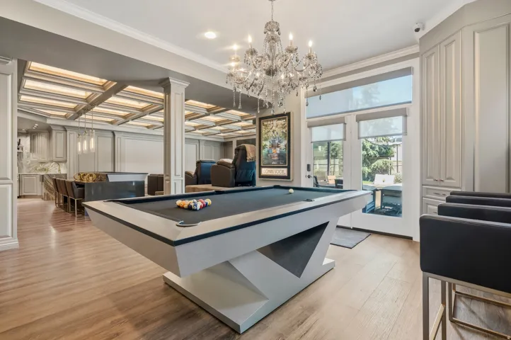Open-concept entertainment space featuring a contemporary pool table, wood-finish flooring, and an ornate crystal chandelier