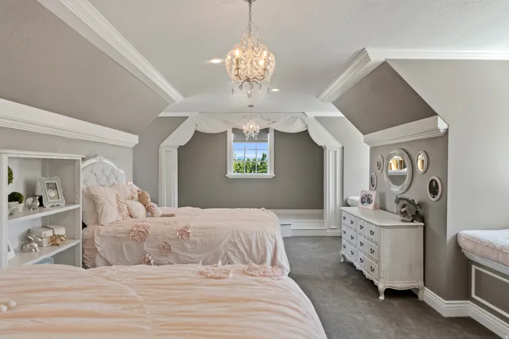 Attic room featuring a window with exterior scenery, sloped ceilings, crown molding, and two chandeliers