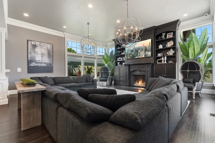 Spacious living area featuring dark wood-finish flooring, a built-in media cabinet with fireplace, recessed lighting, and large picture windows
