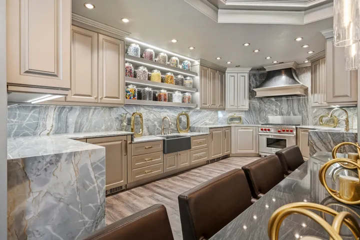 Gourmet kitchen featuring a built-in range, custom range hood, expansive stone countertops, full-height stone backsplash, and wood-finish flooring