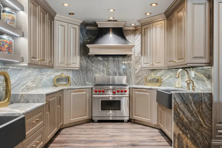 Gourmet kitchen featuring a professional-grade stainless steel range with red knobs, custom range hood, full-height stone slab backsplash, integrated under-cabinet lighting, and recessed ceiling lighting