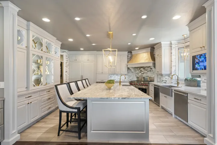 Gourmet kitchen featuring a substantial central island with seating, a gold-toned range hood, and a built-in stainless steel range