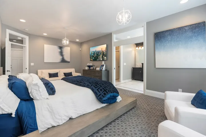 Spacious room featuring patterned carpeting, recessed lighting, and a wide entryway to an adjacent bathroom with a dark wood vanity and wall-mounted light fixture
