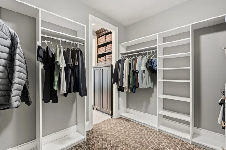 Walk-in closet featuring custom white built-in shelving, hanging rods, and patterned carpet flooring