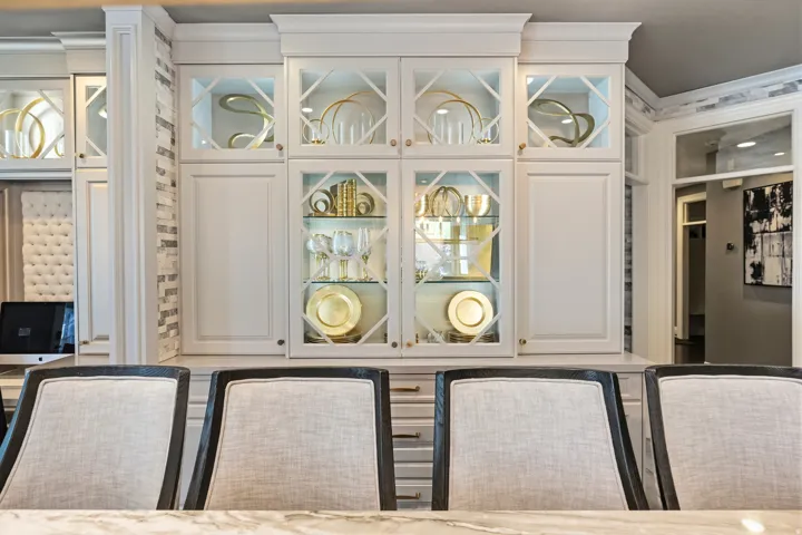 Custom built-in cabinetry featuring glass-front doors with geometric mullions, interior lighting, and a base cabinet with drawer storage