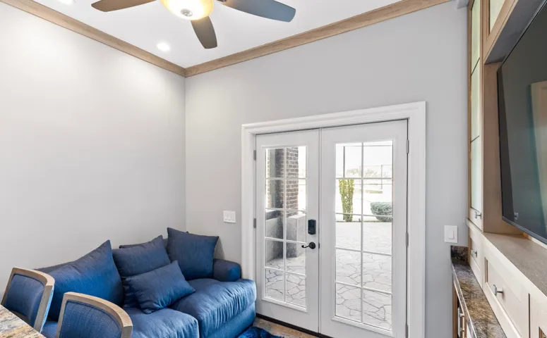 Double glass-paneled doors opening to an outdoor patio with stone pavers, featuring a ceiling fan with integrated lighting, recessed ceiling lights, and custom built-in cabinetry with a countertop
