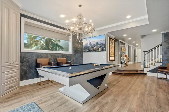 Recreation space featuring wood-finish flooring, a contemporary chandelier, recessed lighting, built-in cabinetry, and a large window with roller shades