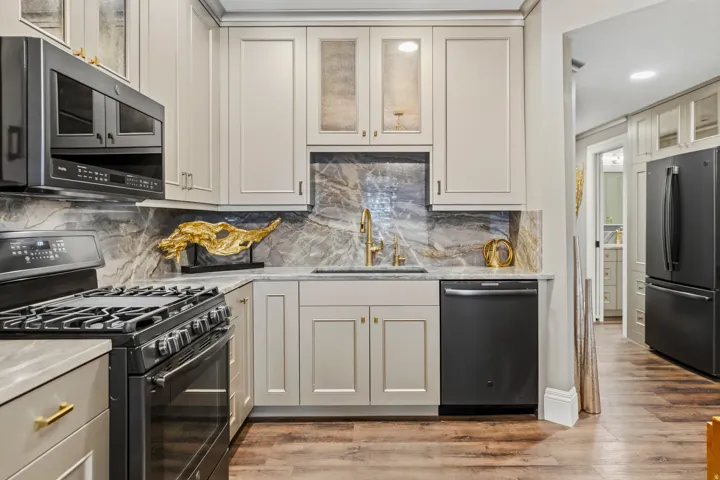 Modern kitchen featuring light cabinetry with gold-finish hardware, black stainless steel appliances, a gas range with an overhead microwave, and a grey and brown veined backsplash